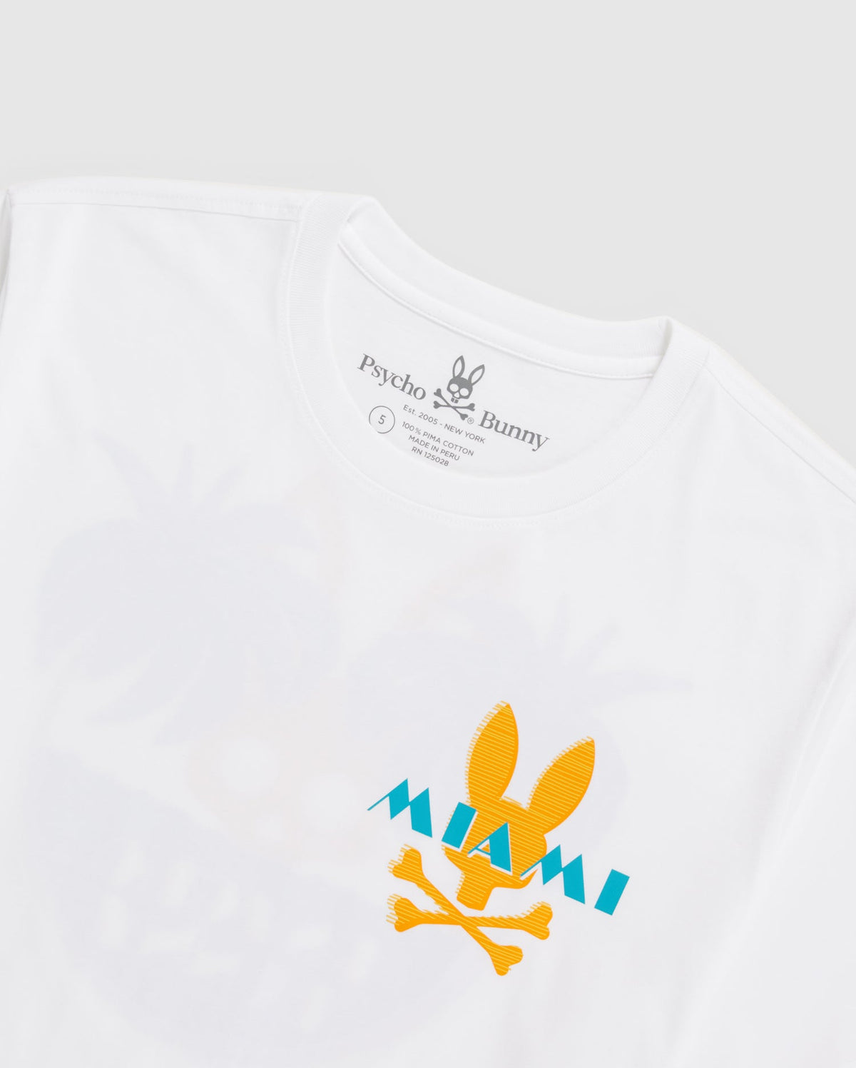 A white men's MENS MIAMI TEE - B6U550W1PC featuring a yellow bunny skull and crossbones with "MIAMI" written in turquoise over it, crafted from soft Pima cotton. The shirt's label reads "Psycho Bunny." The background is a light gray.