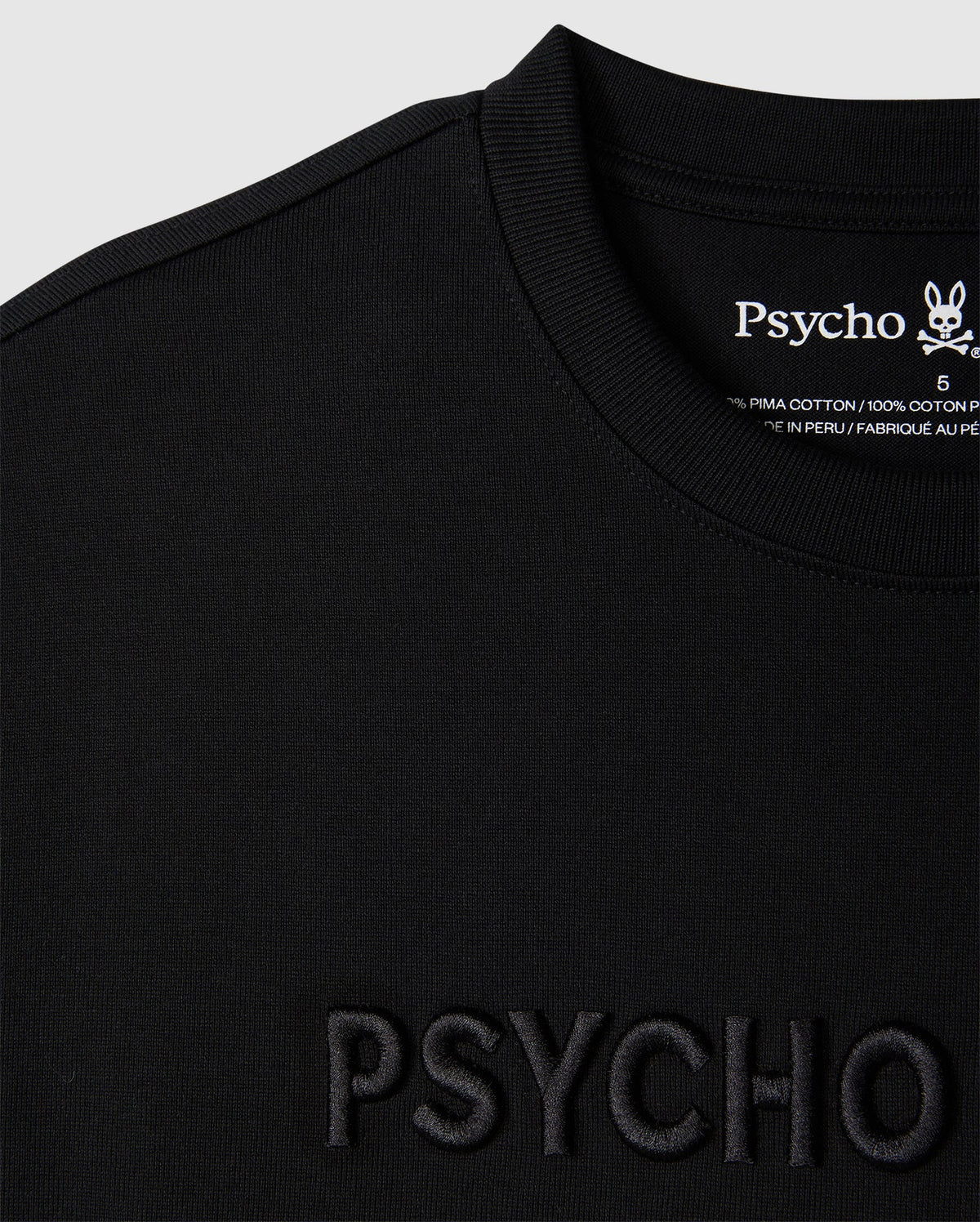Close-up of a black relaxed fit MENS WINDCREST HEAVY WEIGHT TEE with the word "psycho" embossed on the front and a tag on the back neckline with the embroidered logo and fabric details from Psycho Bunny.