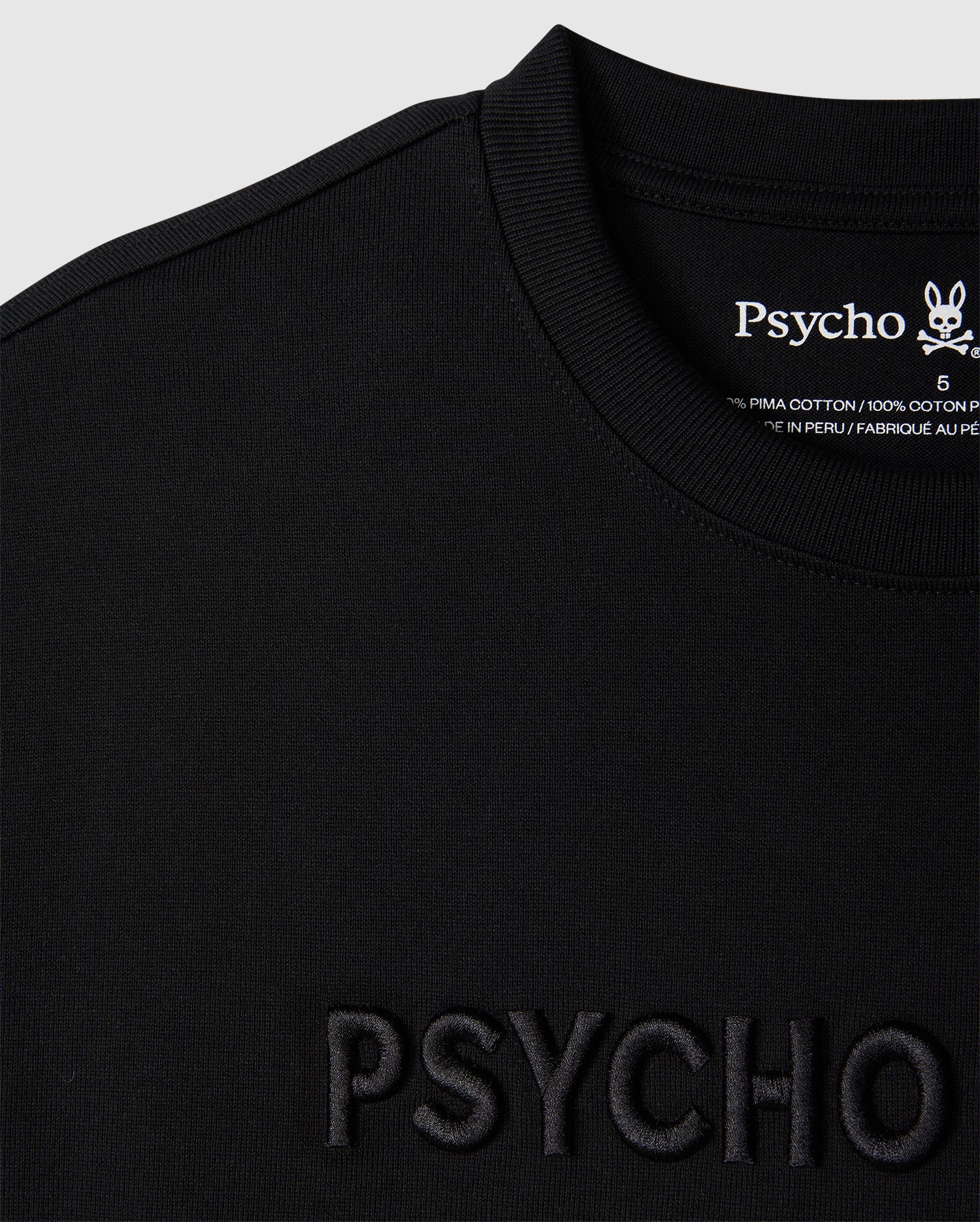 Close-up of a black relaxed fit MENS WINDCREST HEAVY WEIGHT TEE with the word "psycho" embossed on the front and a tag on the back neckline with the embroidered logo and fabric details from Psycho Bunny.