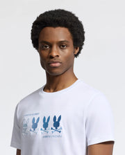 Wearing the Psycho Bunny MENS OCEANIA EMBROIDERED GRAPHIC TEE, a playful retro design pops on a light gray Pima Cotton backdrop, featuring four embroidered bunnies: two blue and one gray adorned with skulls and crossbones.