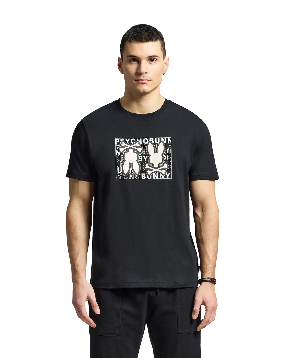 A young man wears a Psycho Bunny MENS GOLD COAST GRAPHIC TEE, featuring Pima cotton and two abstract bunny figures with "Psycho Bunny" on the front, reflecting premium craftsmanship against a plain white background.