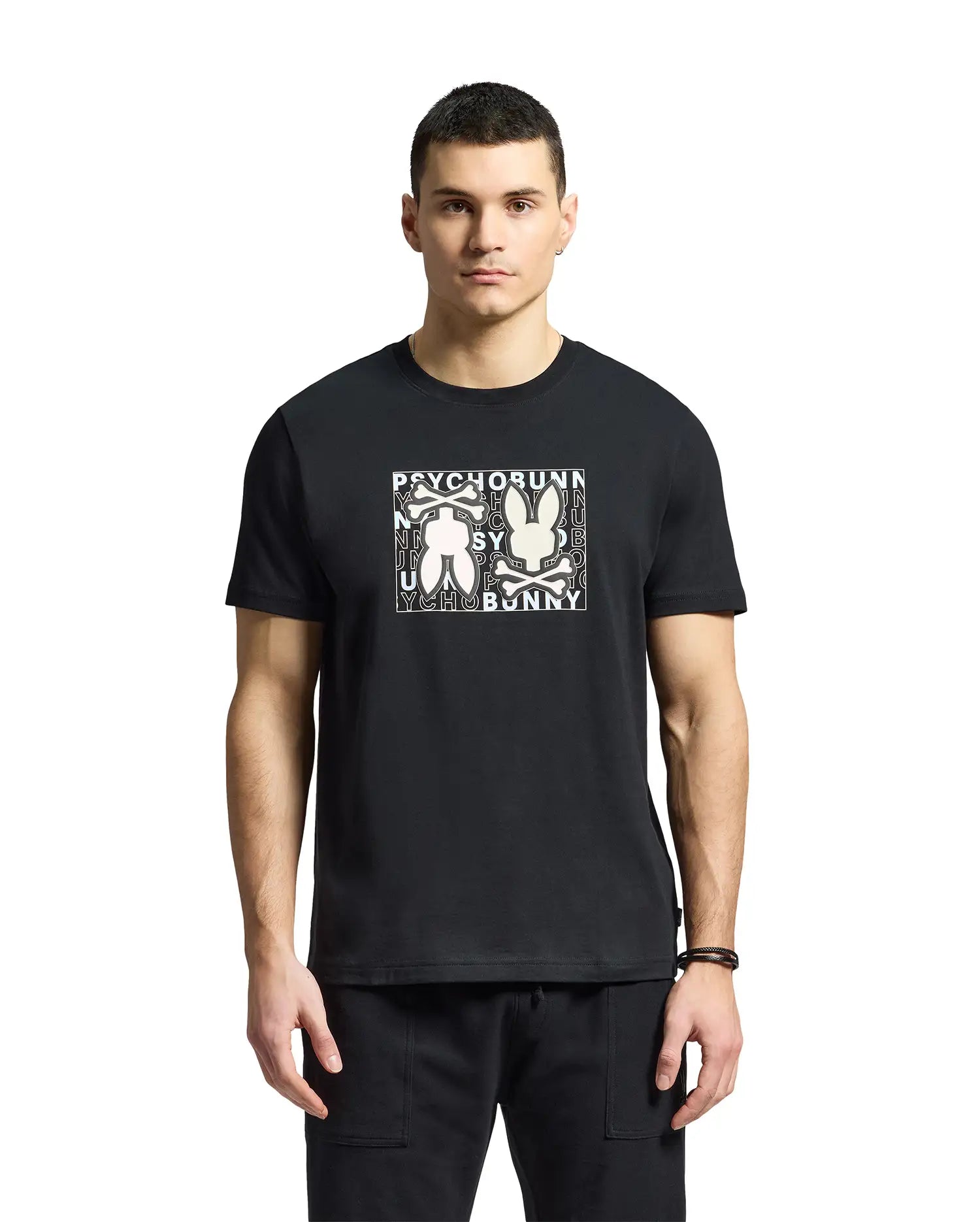 A young man wears a Psycho Bunny MENS GOLD COAST GRAPHIC TEE, featuring Pima cotton and two abstract bunny figures with "Psycho Bunny" on the front, reflecting premium craftsmanship against a plain white background.