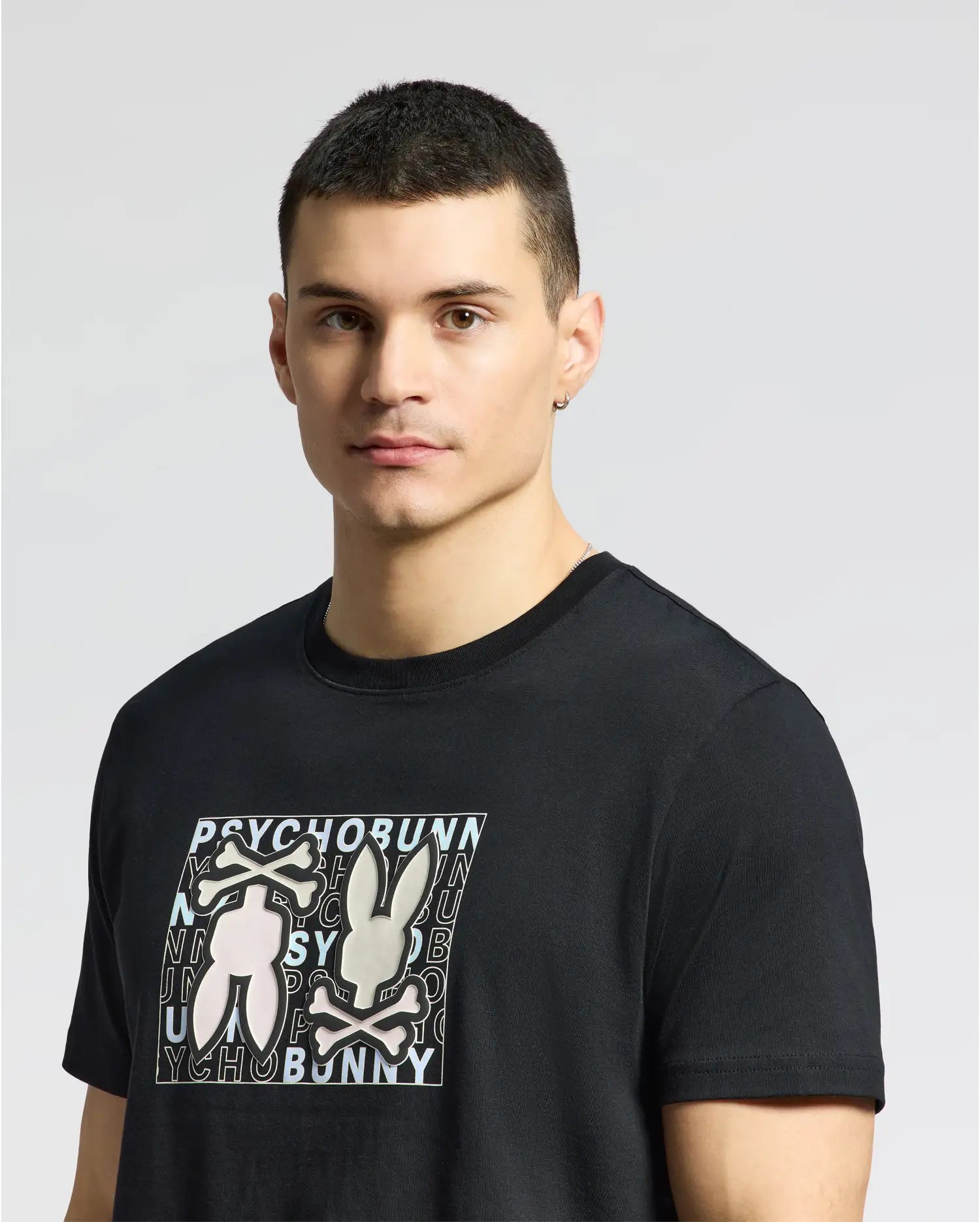 A person with short hair models the MENS GOLD COAST GRAPHIC TEE - B6U631F200, a classic fit black Pima cotton t-shirt by Psycho Bunny, featuring two rabbits and "PSYCHO BUNNY" text, against a plain background.