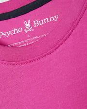 Close-up of a pink Psycho Bunny Mens Pearland Back Graphic Tee (B6U632C200) with an embroidered white label inside the collar. The label features the Psycho Bunny logo, a bunny skull with crossbones, and material information, indicating the shirt is made of 100% Pima cotton.
