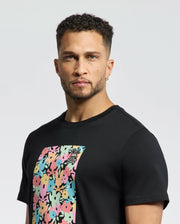 A man with short curly hair and a beard wears the MENS LEMMON GRAPHIC TEE by Psycho Bunny featuring a vibrant floral design and subtle bunny graphic, ensuring all-day comfort with its soft Pima cotton fabric as he stands against a plain white background.