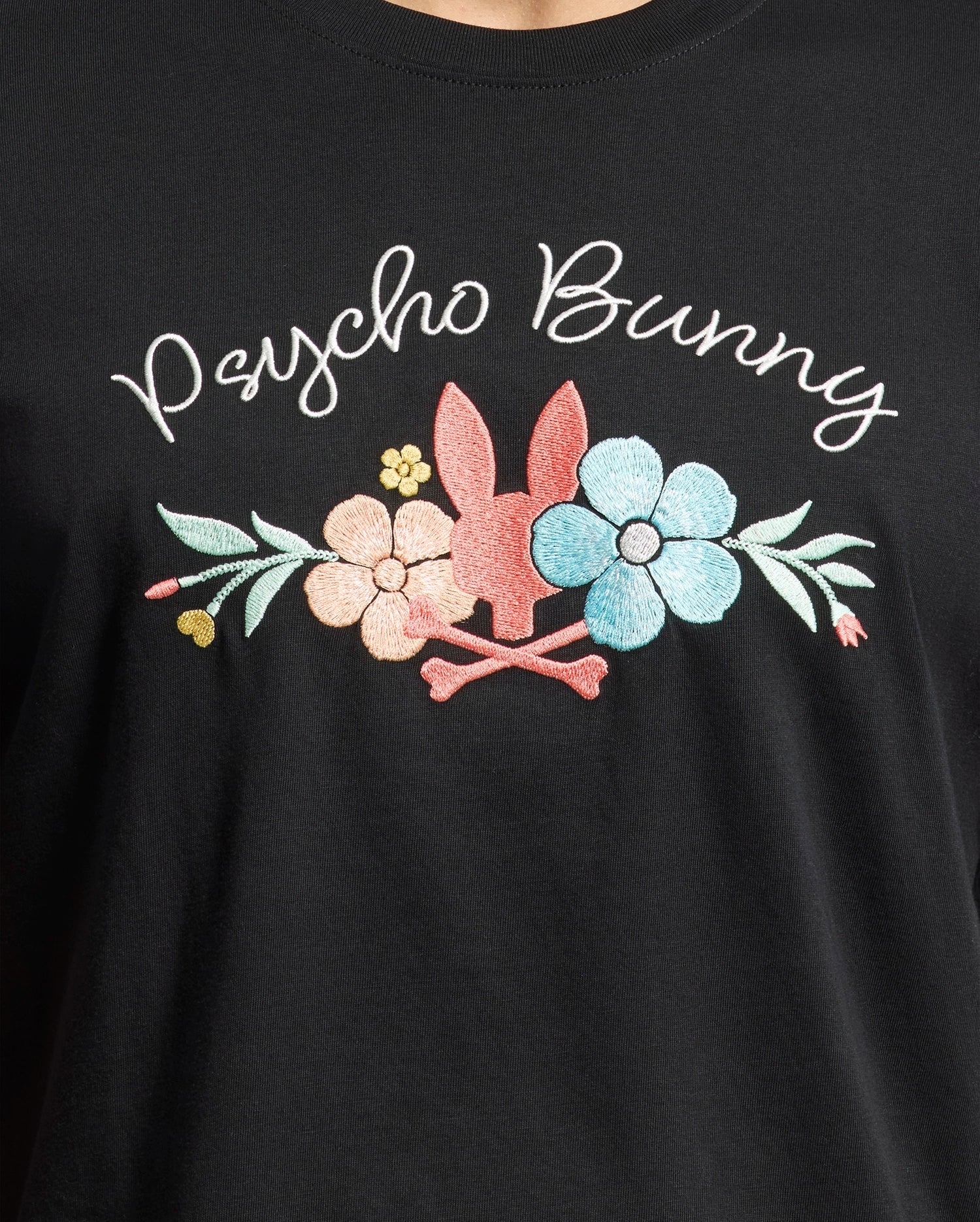 The MENS MEYLON GRAPHIC TEE by Psycho Bunny features soft black Pima cotton with white "Psycho Bunny" text, a playful pink bunny head with crossbones, and colorful pastel flowers in pink, blue, and yellow.