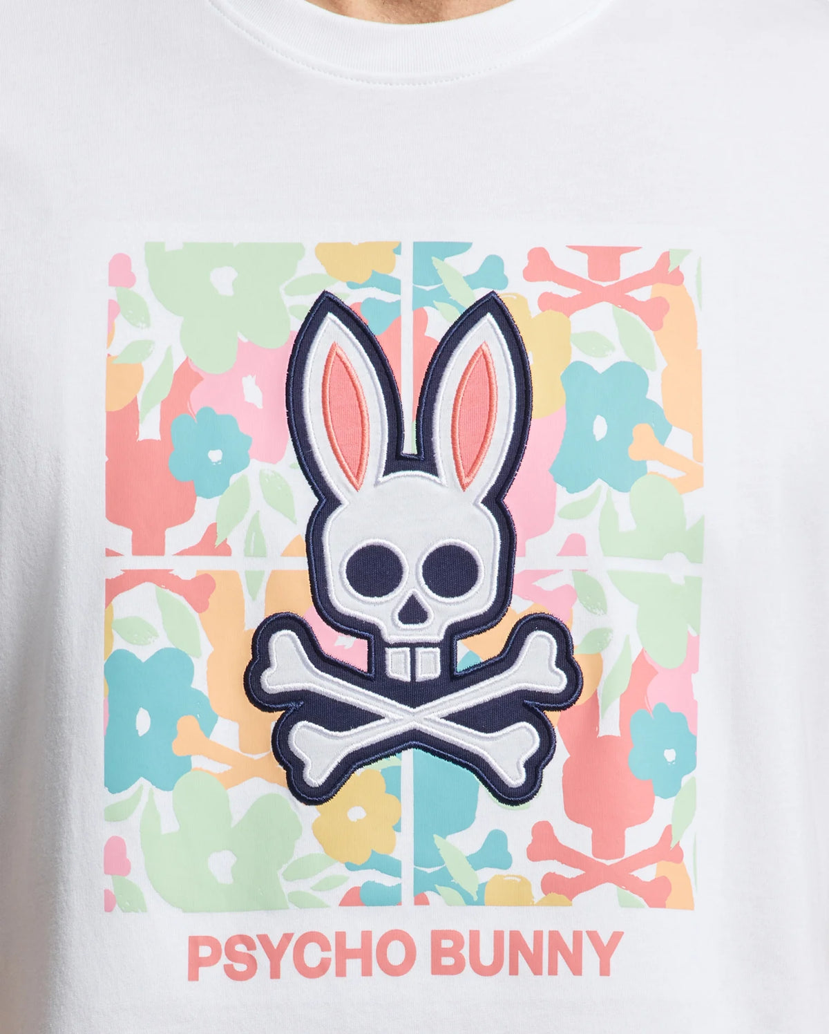 The Psycho Bunny MENS LEMORA GRAPHIC TEE (B6U657F200) in Pima cotton features a skull and crossbones graphic shaped like a bunny’s head with large ears, adorned with pastel pink, blue, and green flowers. "PSYCHO BUNNY" is boldly printed beneath this water-based masterpiece.