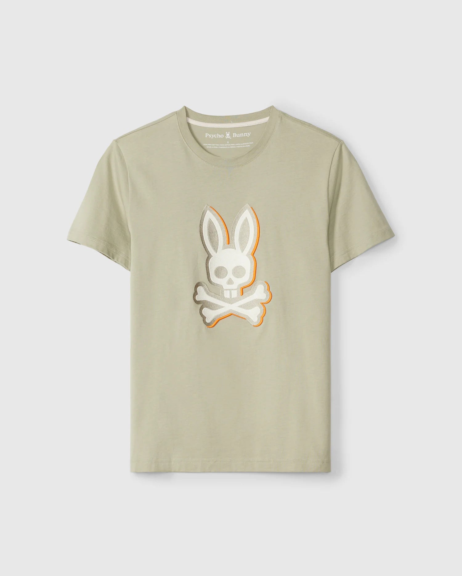 A light beige MENS KAYDEN GRAPHIC TEE - B6U676C200 featuring a stylized design of a skull with bunny ears and crossbones on the front center. Made from soft Pima cotton, the t-shirt displays the brand label "Psycho Bunny" inside the collar. The t-shirt is showcased against a plain white background.