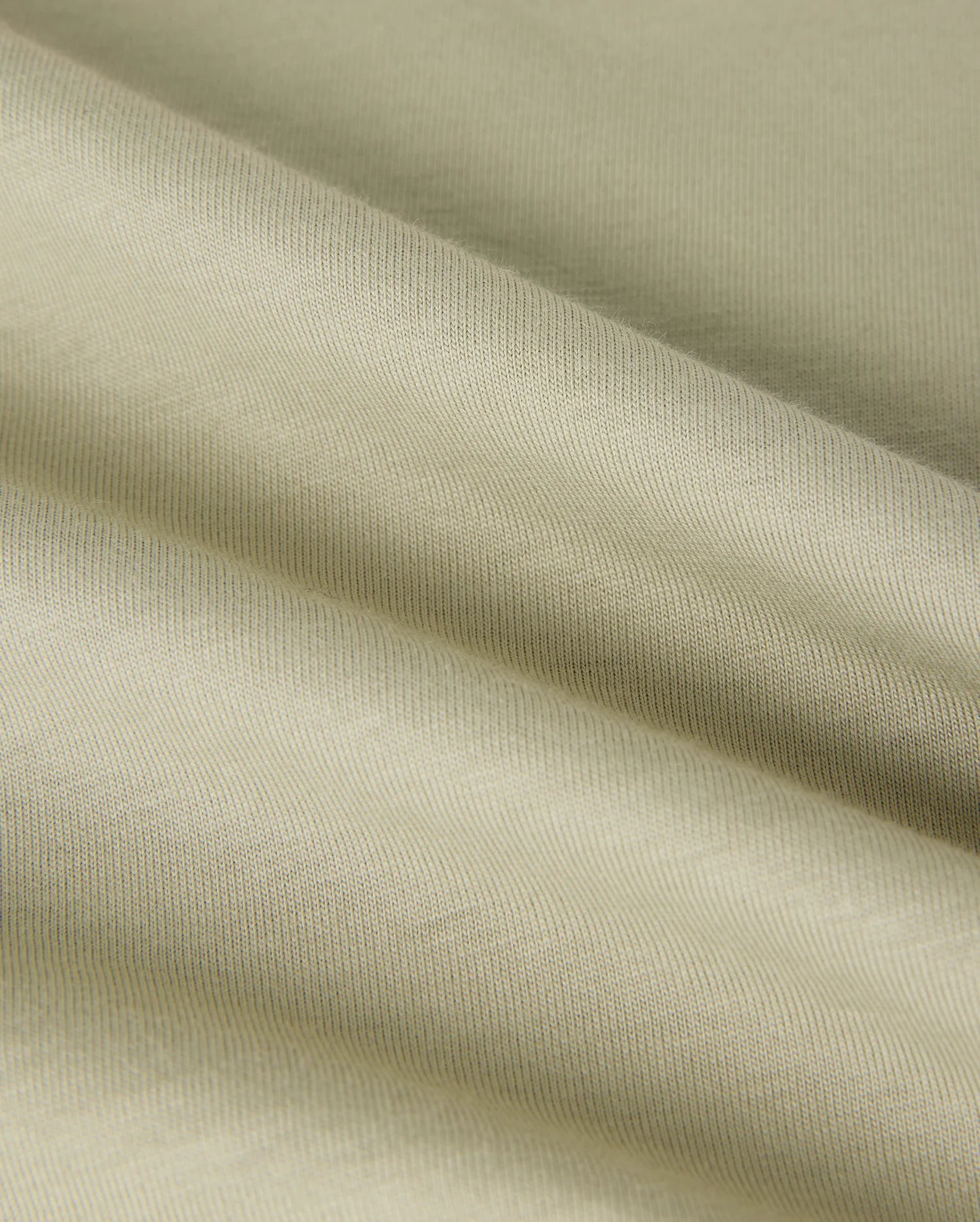 A close-up image of a light beige, textured Pima cotton fabric with visible folds creating soft shadows. The fabric appears smooth with a fine weave, showcasing its subtle sheen and gentle draping, reminiscent of the luxurious quality found in a Psycho Bunny MENS KAYDEN GRAPHIC TEE - B6U676C200.