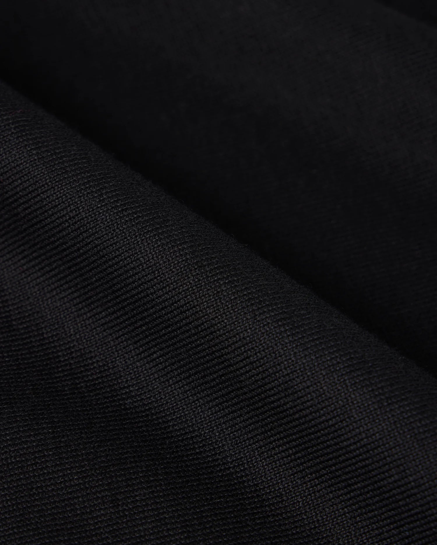 Close-up image of black fabric with visible texture from Psycho Bunny's MENS DUKE OVERSIZED TEE - B6U742D200. The material appears to be folded, creating soft, undulating lines and showcasing its smooth surface and fine weave, reminiscent of a relaxed fit Pima cotton tee.