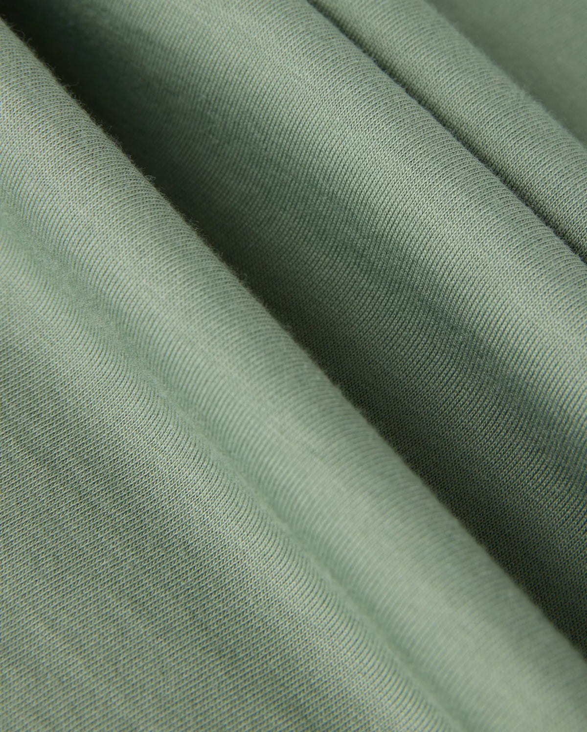 Close-up view of a smooth, green fabric with a subtle texture, characteristic of luxurious Pima cotton. The folds create gentle shadows, emphasizing the material's soft and slightly ribbed surface—ideal for crafting the high-quality MENS MALTON GRAPHIC TEE - B6U795D200 by Psycho Bunny.
