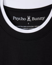 Close-up of a black and white double collar T-shirt, identified as the "MENS CAMPO POCKET TEE - B6U801D200," featuring a label with "Psycho Bunny" text and a bunny logo. The label states that it is made of 100% Pima cotton material and manufactured in Peru.