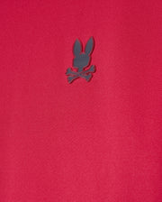 The Psycho Bunny Mens Edmonds Sport Tee (B6U857D200) is a red, textured shirt made from quick-drying, antimicrobial fabric with a small, dark emblem of a rabbit head and crossbones.