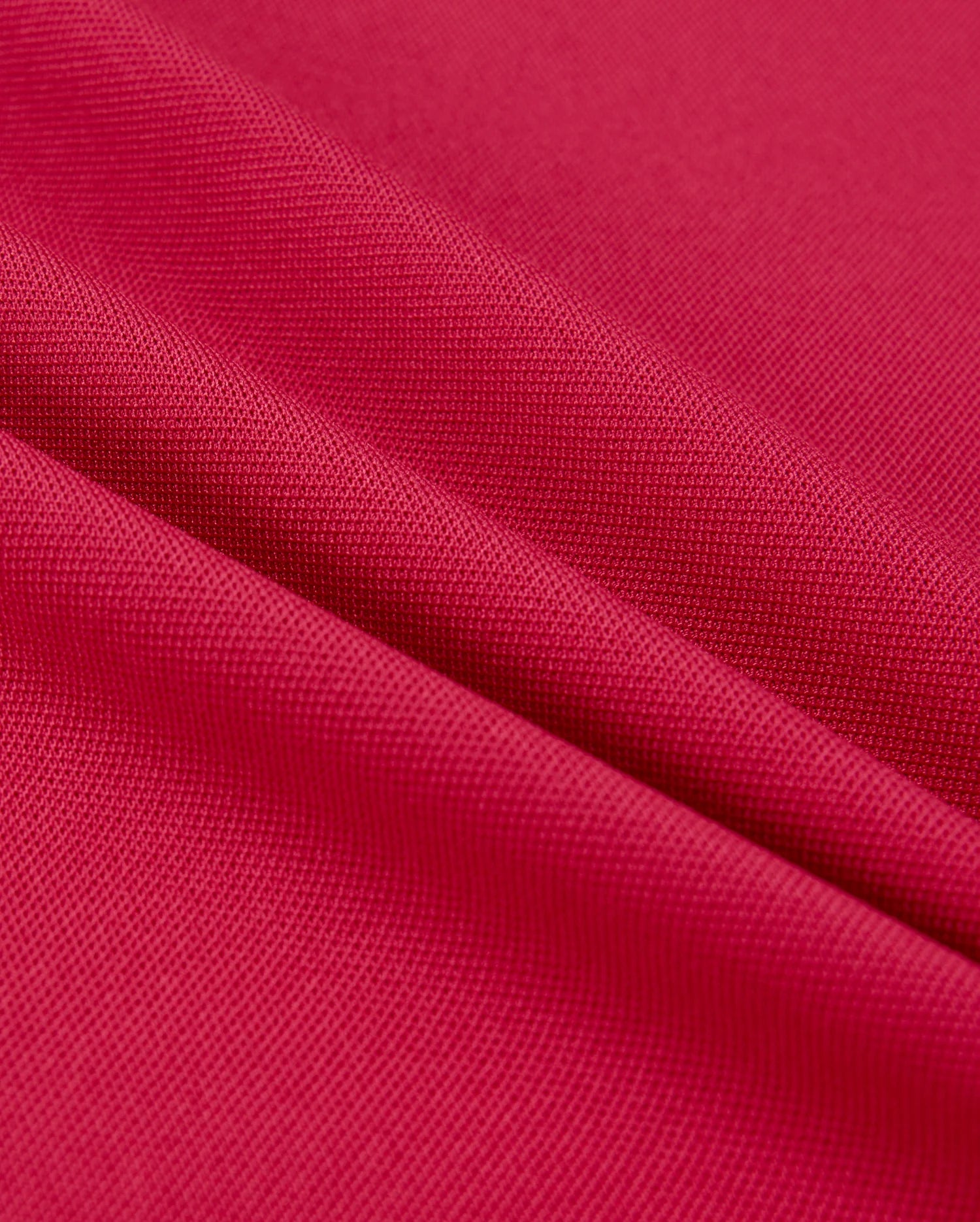 Close-up of vibrant red Psycho Bunny MENS EDMONDS SPORT TEE - B6U857D200 fabric, showing a textured surface with diagonal folds. Lighting highlights the weave, quick-drying properties, and antimicrobial qualities, reminiscent of a sport tee's depth and detail.