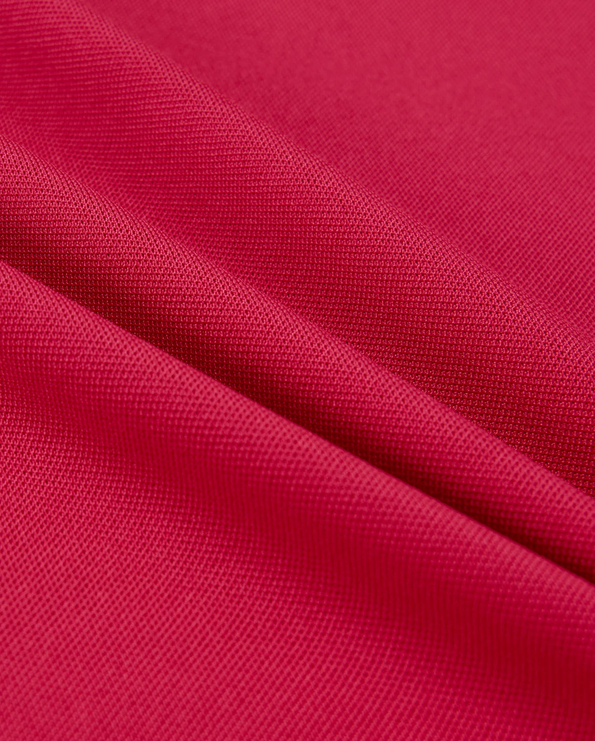 Close-up of vibrant red Psycho Bunny MENS EDMONDS SPORT TEE - B6U857D200 fabric, showing a textured surface with diagonal folds. Lighting highlights the weave, quick-drying properties, and antimicrobial qualities, reminiscent of a sport tee's depth and detail.
