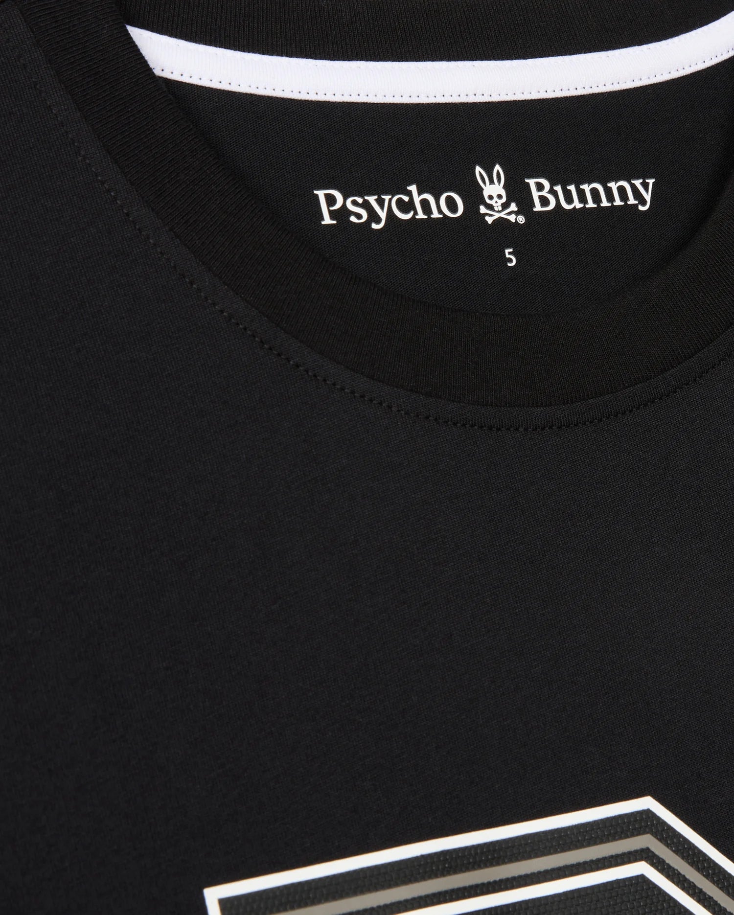 A close-up of a black MENS ZACK GRAPHIC TEE - B6U897D200 by Psycho Bunny featuring a white label inside the collar that reads "Psycho Bunny" with a small bunny logo and crossbones underneath. The number "5" is visible near the label. This Pima cotton shirt has a white stripe along the collar's inner seam.