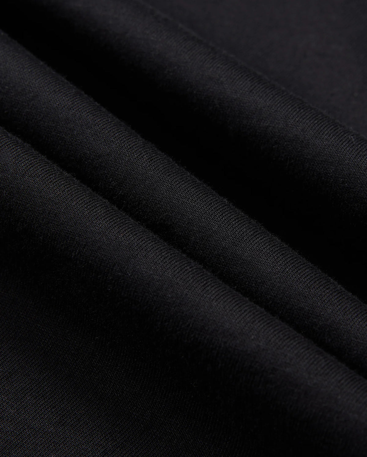 Close-up image of the Psycho Bunny MENS ZACK GRAPHIC TEE - B6U897D200 in black Pima cotton fabric with a smooth texture. The material is shown in folded layers, highlighting the softness and fine weave of the textile. The color is solid black with no visible patterns or designs.