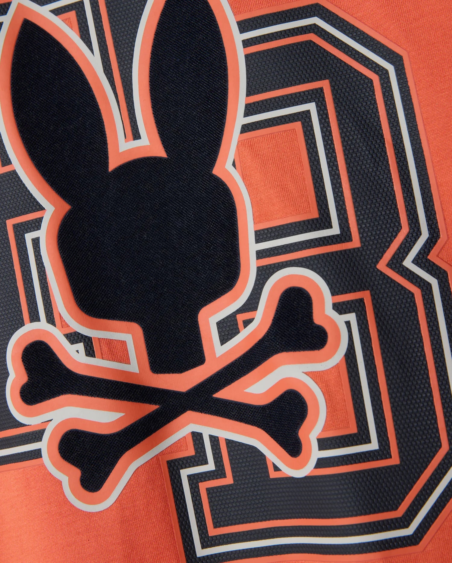 The Psycho Bunny MENS ZACK GRAPHIC TEE - B6U897D200 features an edgy design with a black silhouette of a bunny head and crossed bones, centered over a large "8" on an orange background. This striking tee, made from soft Pima cotton, highlights the bunny and bones outlined in vivid orange and white borders.