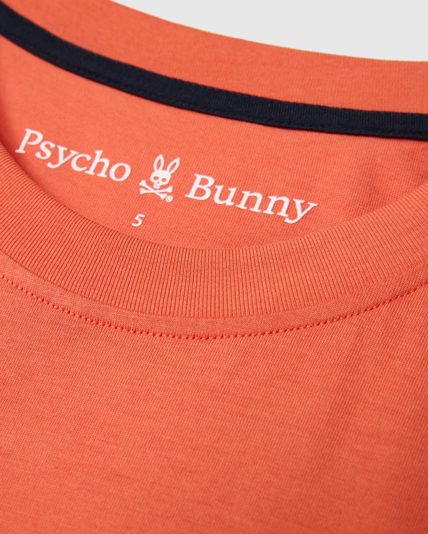 Close-up of the MENS ZACK GRAPHIC TEE by Psycho Bunny, crafted from soft Pima cotton in an orange hue and featuring a black-trimmed collar. The inner fabric showcases the Psycho Bunny brand name, logo, and a size label "S", encapsulating the essence of this standout graphic tee.