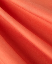 Close-up of the orange fabric from the MENS ZACK GRAPHIC TEE - B6U897D200 by Psycho Bunny, featuring a fine, smooth texture similar to Pima cotton. The material is pleated, creating soft folds and shadows that emphasize its sheen and uniform color.