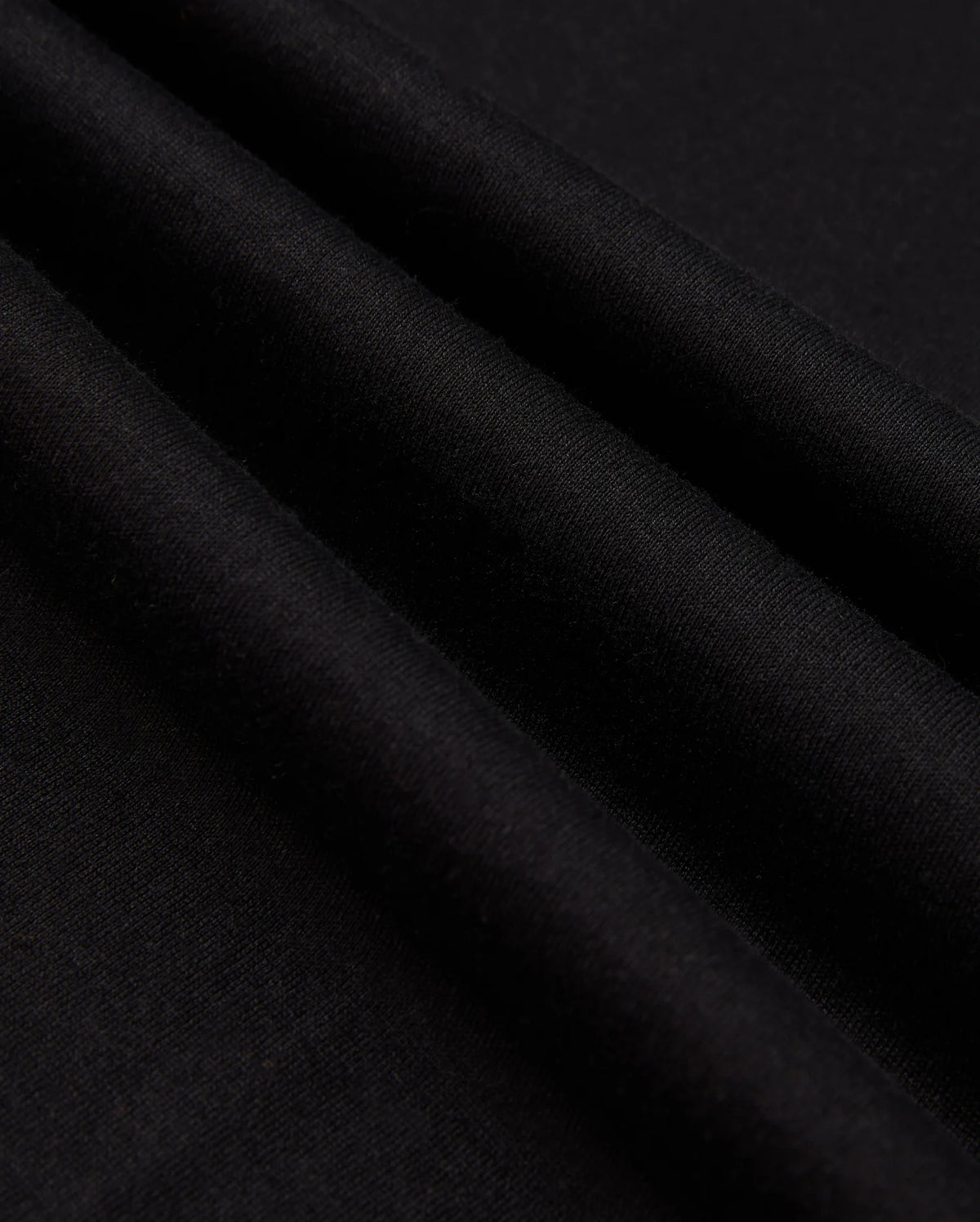 Close-up of the MENS JAMES PREMIUM CREW NECK TEE by Psycho Bunny, crafted from high-quality Pima cotton fabric with a smooth texture and several parallel folds. The surface of the tee is uniformly dark, creating subtle shadows along the meticulous embroidery that adds an elegant touch.