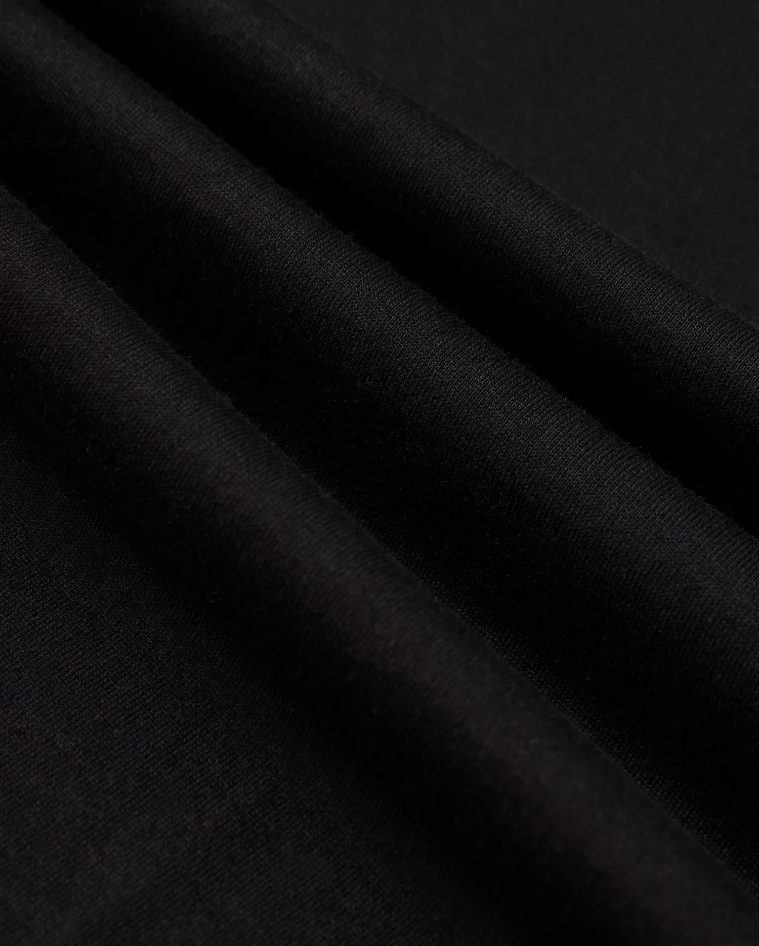 Close-up of the MENS JAMES PREMIUM CREW NECK TEE by Psycho Bunny, crafted from high-quality Pima cotton fabric with a smooth texture and several parallel folds. The surface of the tee is uniformly dark, creating subtle shadows along the meticulous embroidery that adds an elegant touch.