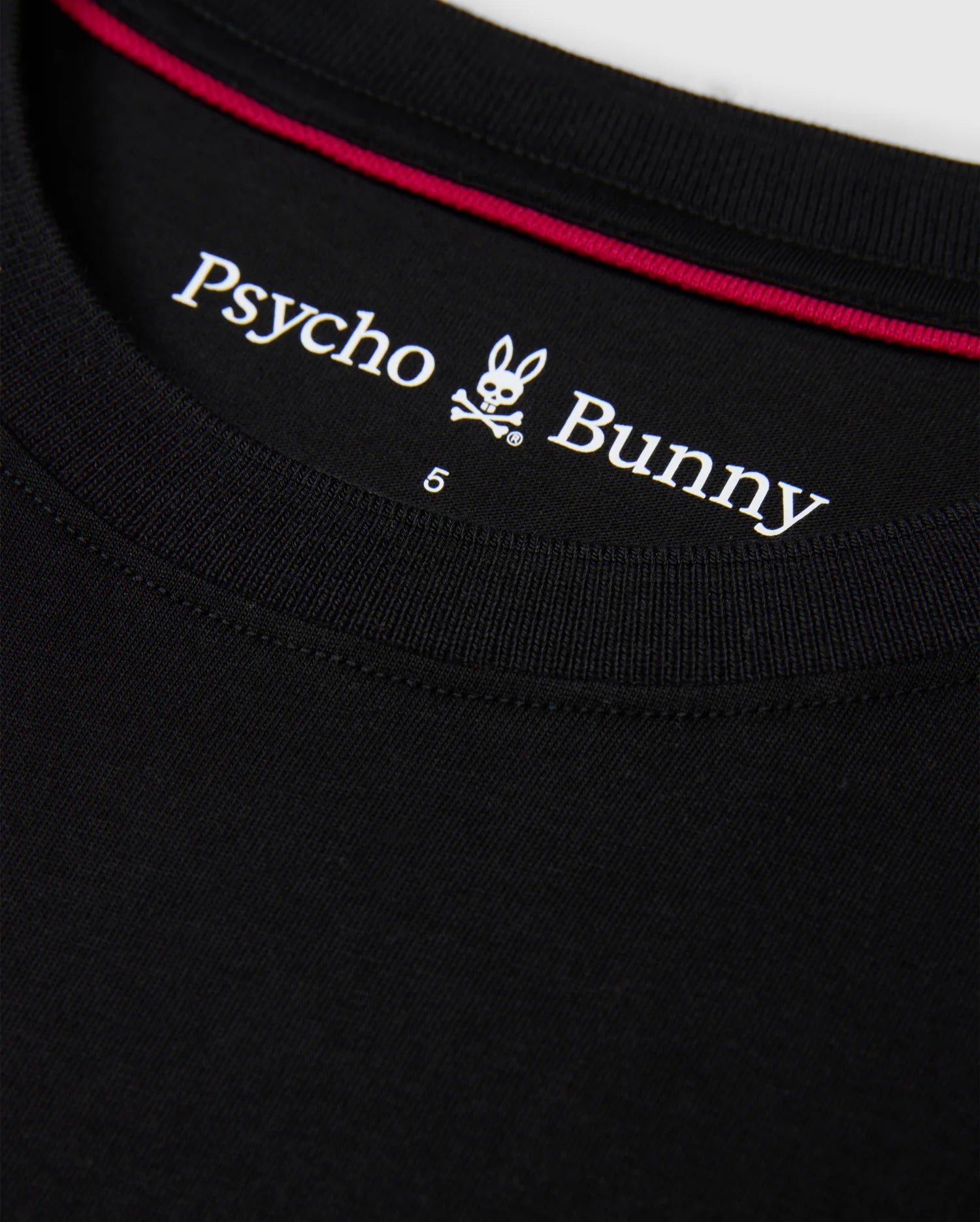 Close-up of the collar of the MENS MALTON FASHION TEE - B6U966D200 in black, showcasing the "Psycho Bunny" logo with its distinctive stylized bunny skull and crossbones, along with a red trim on the inside.