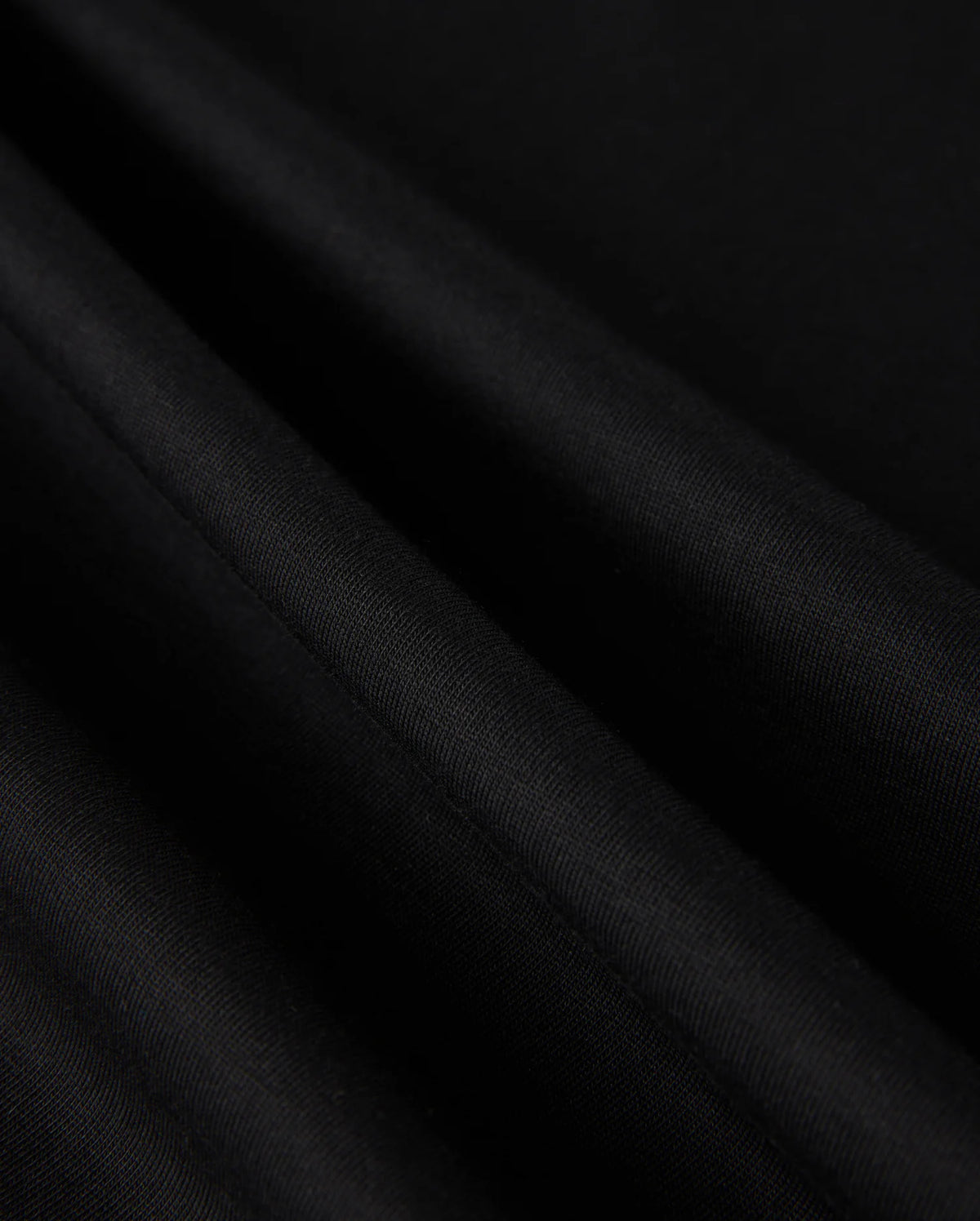 Close-up of the luxe, black fabric from the MENS MALTON FASHION TEE - B6U966D200 by Psycho Bunny, showcasing its smooth pima cotton with visible light reflections and folds, creating an elegant texture ideal for men's fashion.