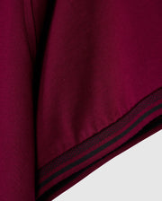A close-up of the maroon fabric with black and green stripes mirrors the stylish design of the MENS MALTON FASHION TEE - B6U966D200 by Psycho Bunny. The thick, slightly textured material fits perfectly within men's fashion tees. Narrow stripes run parallel to the edge, adding a sleek element reminiscent of pima cotton's elegance.