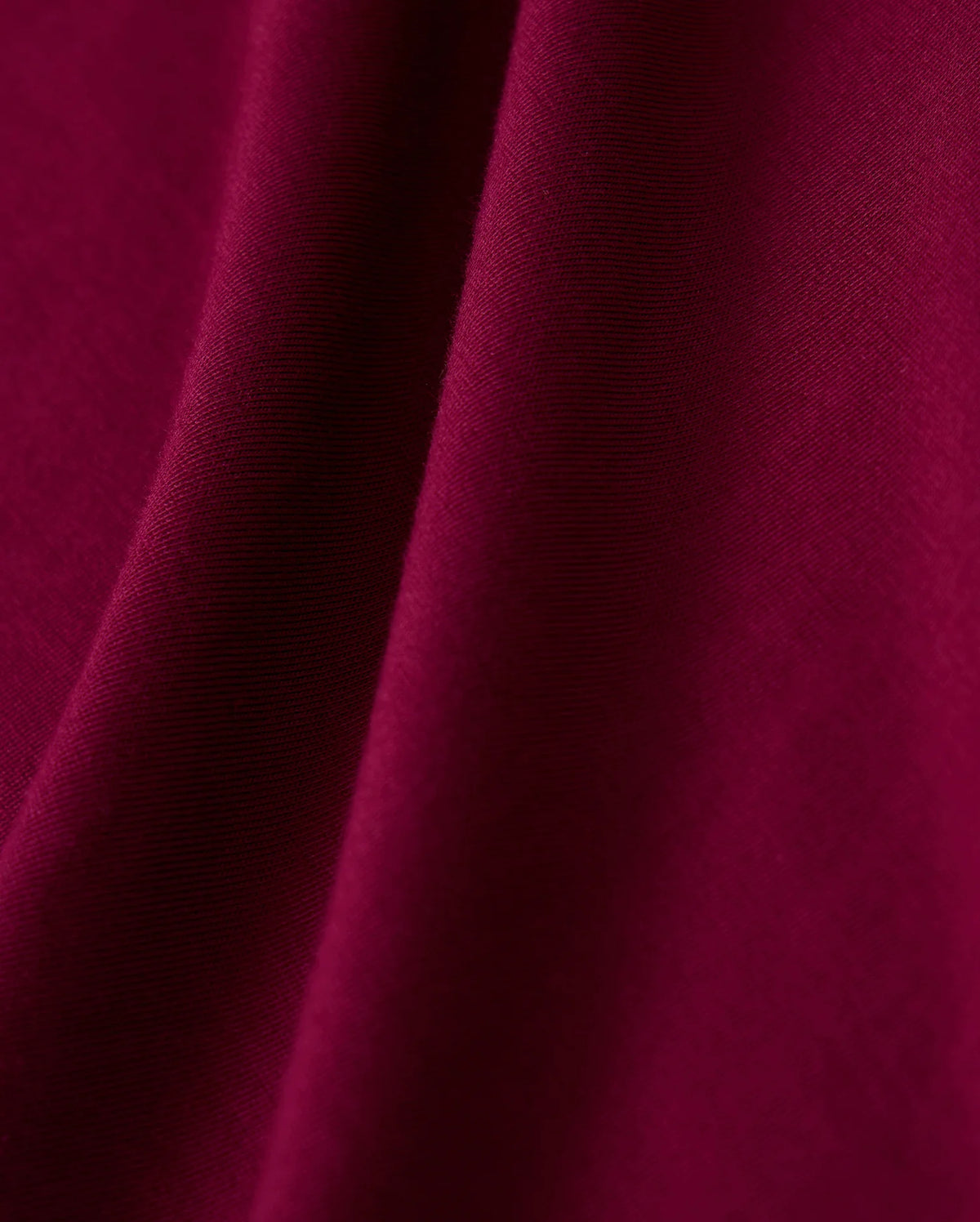The close-up image showcases the rich burgundy fabric of the MENS MALTON FASHION TEE - B6U966D200 by Psycho Bunny, highlighting its soft, flowing folds and smooth texture. The material's surface boasts a subtle sheen, reminiscent of a stylish t-shirt made from the finest pima cotton, exuding a luxurious and elegant appearance.