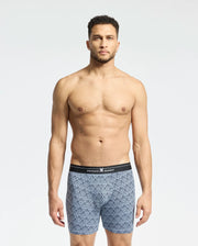 A man is shown in a plain white background wearing one of the MENS 2 PACK BOXER BRIEF - B6V481F200 by Psycho Bunny, with a black waistband displaying "Psycho Bunny." Crafted from a stretchy Pima cotton-Modal blend, these blue patterned boxer briefs ensure comfort.