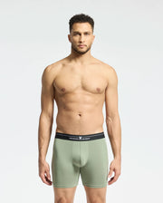 A man in a plain setting models light green Psycho Bunny boxer briefs with a black waistband featuring small text. Crafted from a stretchy Pima cotton-Modal blend, these MENS 2 PACK BOXER BRIEF - B6V481F200 offer all-day comfort as he gazes at the camera with a neutral look.