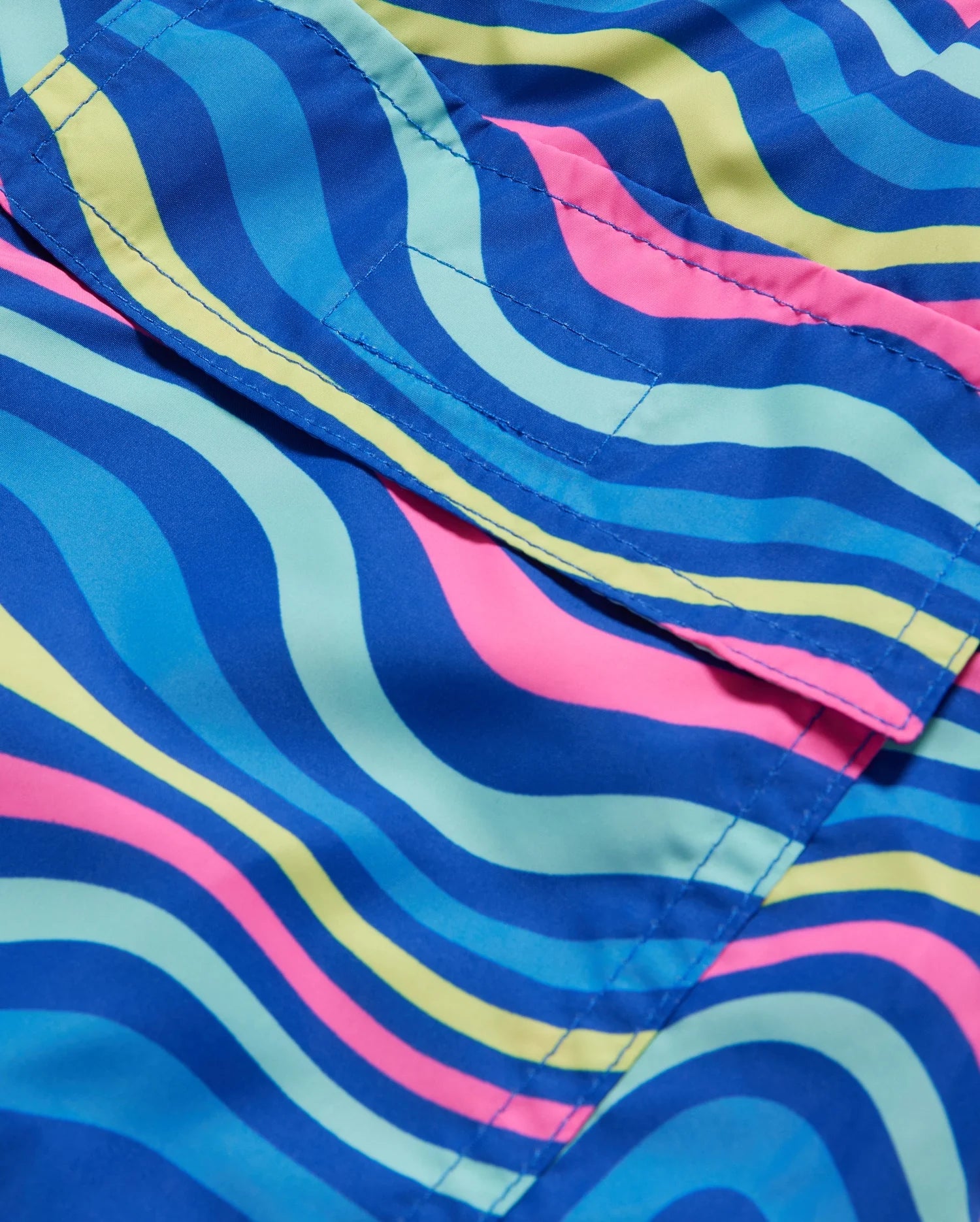 A close-up of fabric with a vibrant wave-like pattern in blue, green, yellow, and pink. The material has visible stitching and folds, displaying overlapping bands of color flowing in curves. The texture appears smooth and shiny, reminiscent of high-quality Psycho Bunny MENS CLARKSON LIGHTWEIGHT SWIM TRUNK - B6W120B2SW.