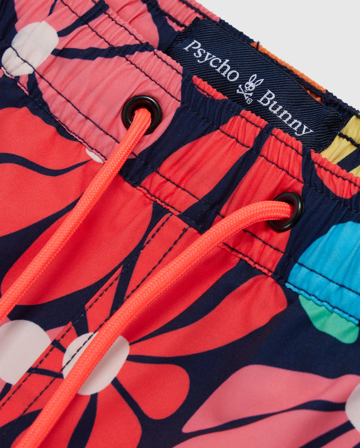 Close-up of MENS MENTZ SWIM TRUNK - B6W320B2SW by Psycho Bunny featuring a vibrant floral pattern in red, blue, yellow, and white hues. The waistband has a dark blue elastic band with a white Psycho Bunny logo and neon orange drawstrings.