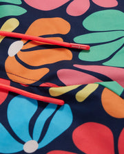 A close-up of vibrant, multicolored floral pattern swimwear fabric, featuring predominantly orange, blue, pink, and green hues. Two bright red drawstrings are placed diagonally over the quick-dry **Psycho Bunny MENS MENTZ SWIM TRUNK - B6W320B2SW** fabric with "Psycho Bunny" written on the tips of the drawstrings.