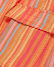 Close-up of a brightly colored fabric with a pattern of vertical stripes in various shades of orange, pink, and blue. The fabric appears to be part of MENS ANTON ALL OVER PRINT SWIM TRUNK - B6W542C200 by Psycho Bunny, with a visible pocket and stitching details.