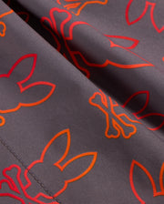 Close-up of Psycho Bunny's MENS SHELDON ALL OVER PRINT SWIM TRUNK - B6W588C200 in grey, featuring a pattern of red and orange outlines of bunny faces and crossed bones. The detailed stitching on the quick-dry fabric is visible, adding texture to the smooth material.