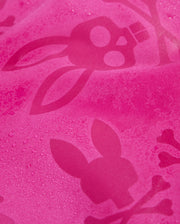 A close-up of quick-drying pink MENS PARKER HYDROCHROMIC SWIM TRUNK - B6W646C200 by Psycho Bunny, featuring a bunny pattern with skulls and crossbones. The swim trunk fabric appears to be slightly wet, with droplets of water visible on the surface. The design elements are in a darker shade of pink, creating a subtle contrast.