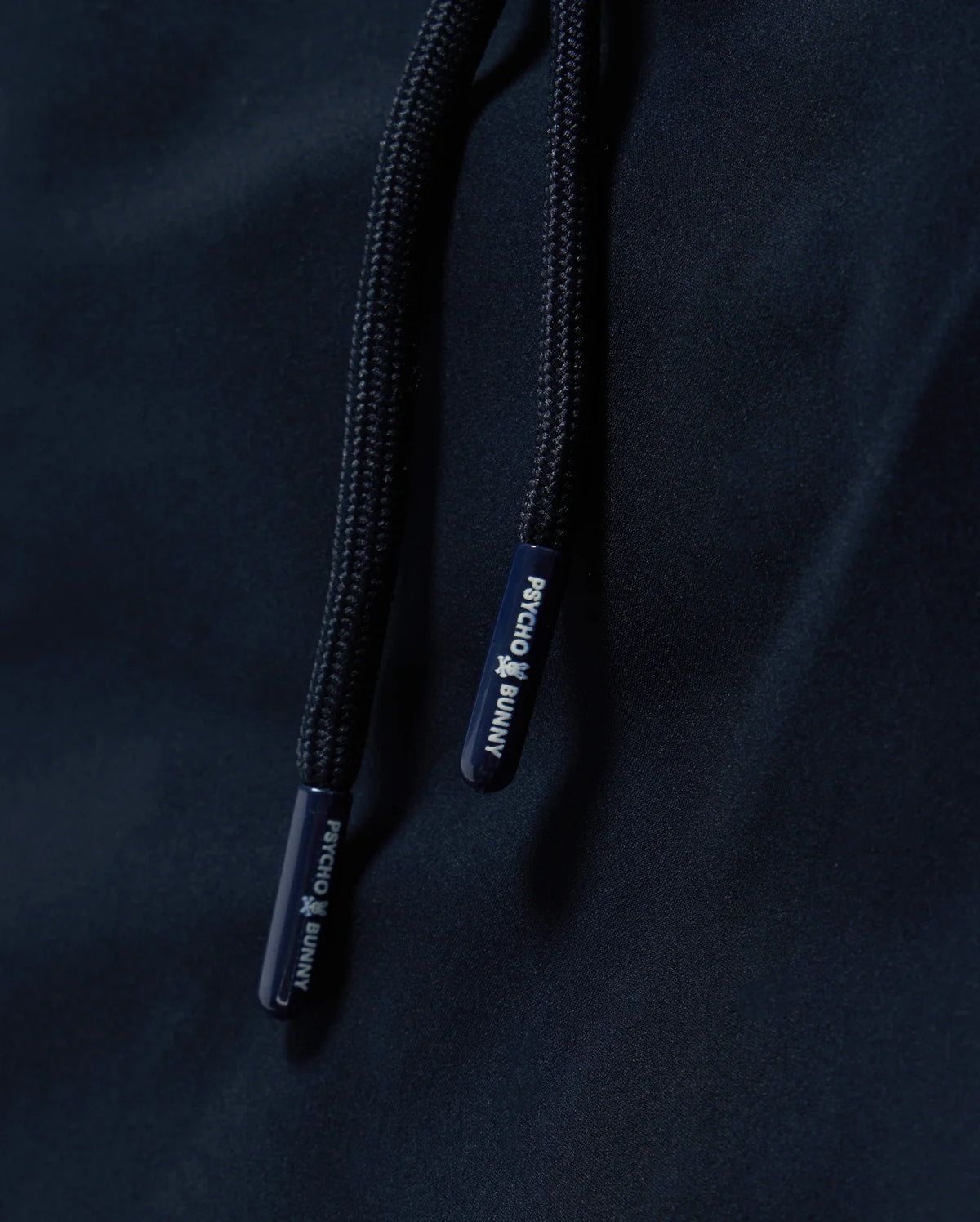 Close-up image of navy blue drawstrings on a fabric surface, with the brand name "Psycho Bunny" printed on the ends in white text. The MENS MELVIN SWIM TRUNK - B6W665C200 features a quick-dry outer shell and a comfortable drawstring stretch waistband for optimal fit and ease.