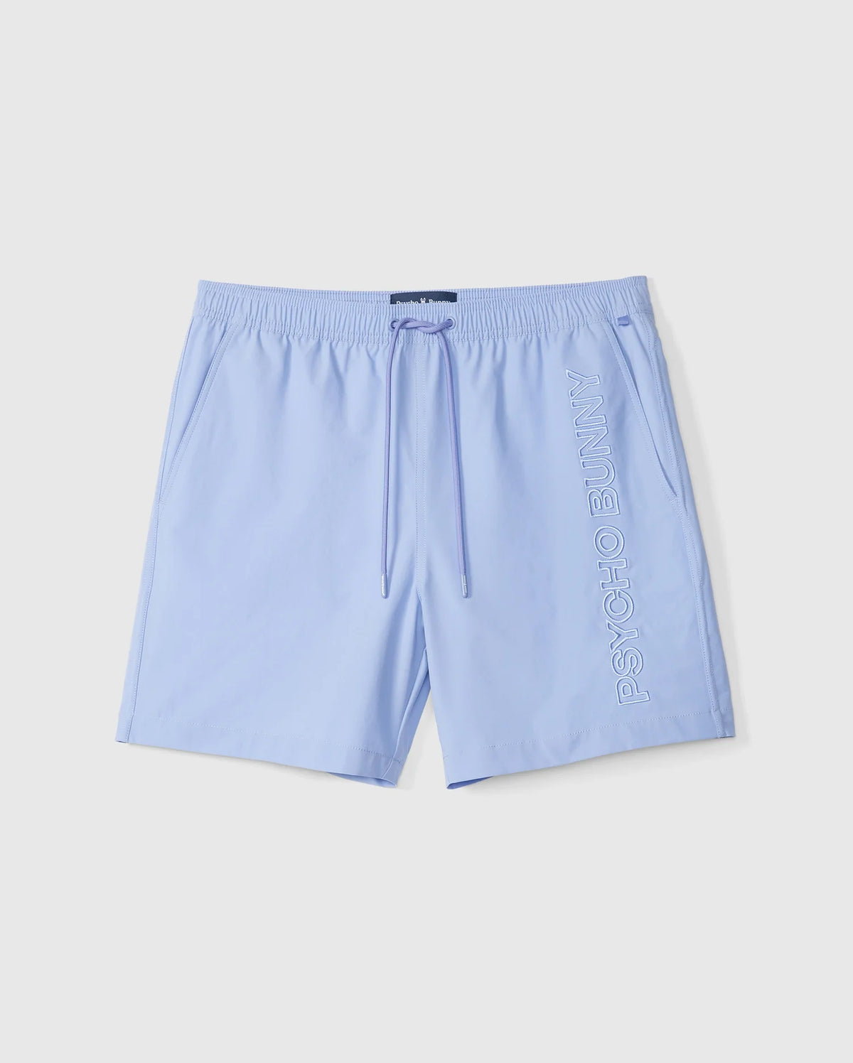 The MENS MELVIN SWIM TRUNK - B6W665C200 by Psycho Bunny features light blue swim trunks with an elastic waistband and drawstring, made from quick-dry textile. Embroidered vertically in white lettering on the right leg are the words "PSYCHO BUNNY." The shorts are laid flat against a white background.