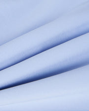 Close-up of the MENS MELVIN SWIM TRUNK - B6W665C200 by Psycho Bunny, showcasing its light blue, quick-dry textile with a smooth and slightly glossy texture. The material is neatly folded in multiple layers, creating soft, diagonal lines and gentle shadows reminiscent of premium swim trunk fabric.