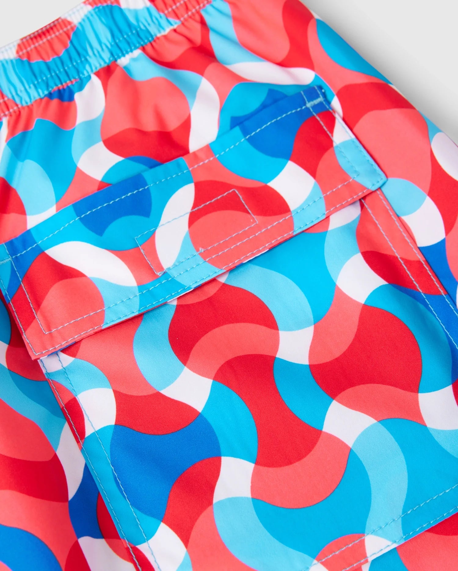 Introducing the Psycho Bunny MENS WALTER LIGHTWEIGHT PRINT SWIM TRUNK - B6W863D200: these shorts showcase a vibrant wavy pattern in red, white, and shades of blue. Crafted from 100% polyester, they feature an elastic waistband and a front flap pocket secured with a velcro closure.