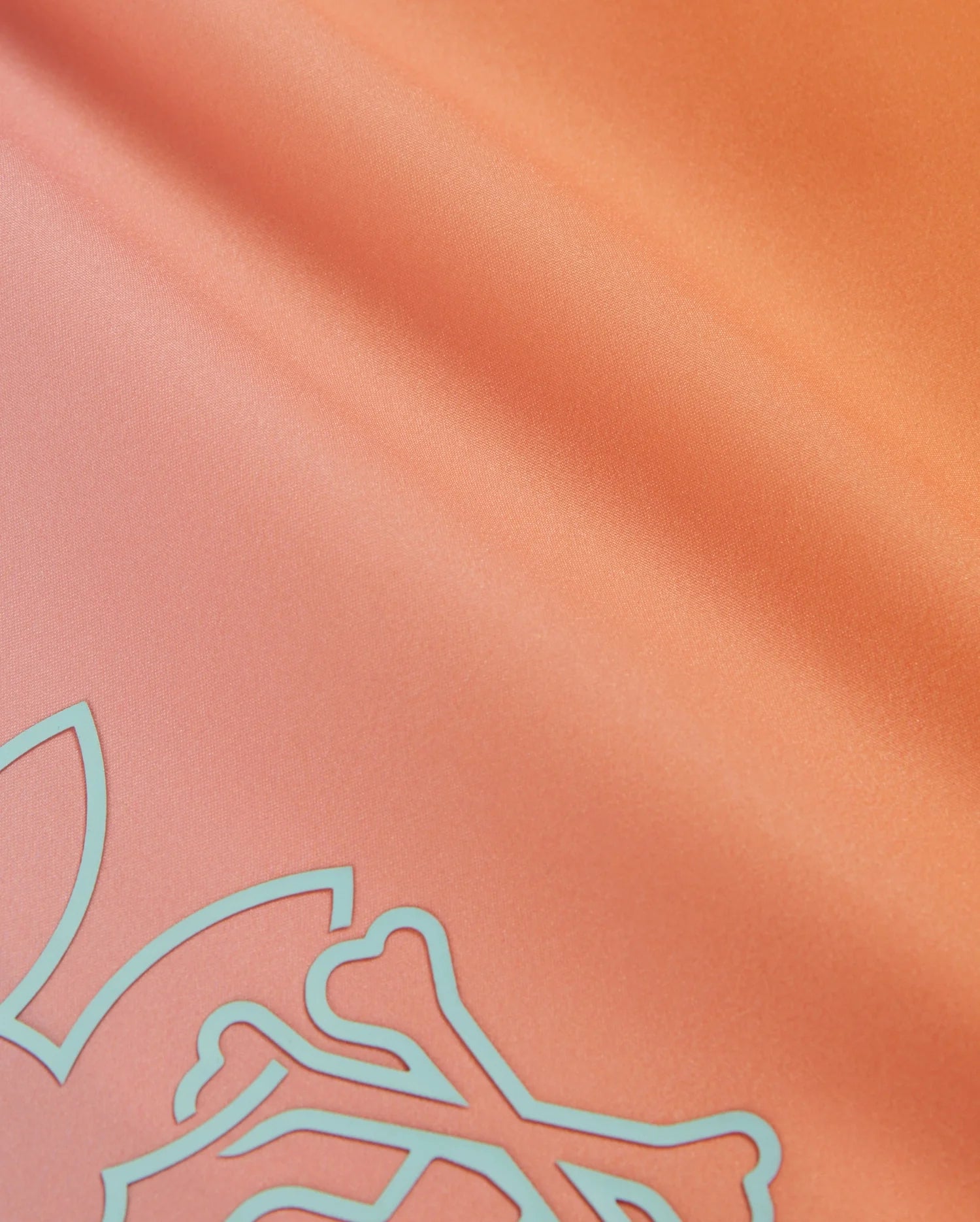 Close-up of silky orange fabric with a smooth texture, featuring a pale blue abstract design in one corner. The fabric has a light sheen, giving it a slightly reflective surface. This HD-printed bunny pattern adds charm, and the material is quick-drying—ideal for the Psycho Bunny MENS WINTON PRINTED SWIM TRUNK - B6W915A2PO.
