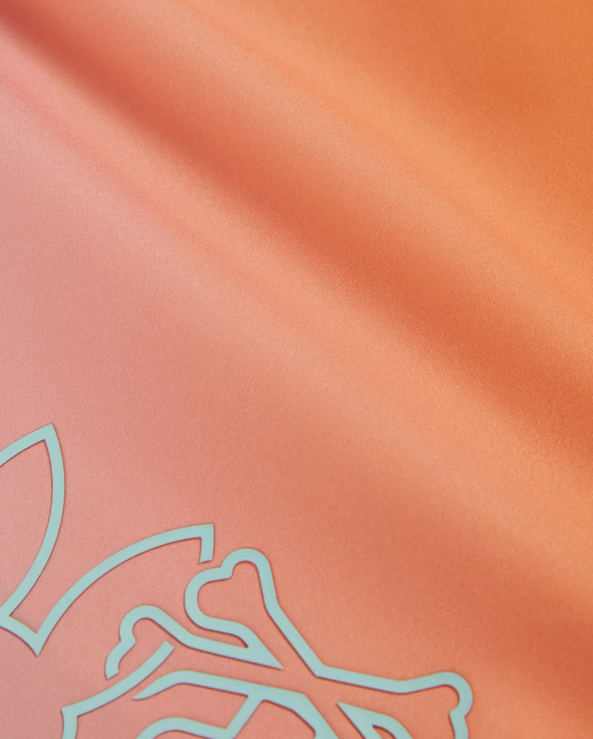 Close-up of silky orange fabric with a smooth texture, featuring a pale blue abstract design in one corner. The fabric has a light sheen, giving it a slightly reflective surface. This HD-printed bunny pattern adds charm, and the material is quick-drying—ideal for the Psycho Bunny MENS WINTON PRINTED SWIM TRUNK - B6W915A2PO.