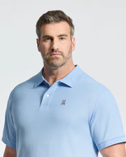 A man with short hair and a beard wears a Psycho Bunny BIG AND TALL CLASSIC PIQUE POLO - B9K001CRPC in light blue, featuring an embroidered logo on the chest. He stands against a plain white background, looking at the camera.