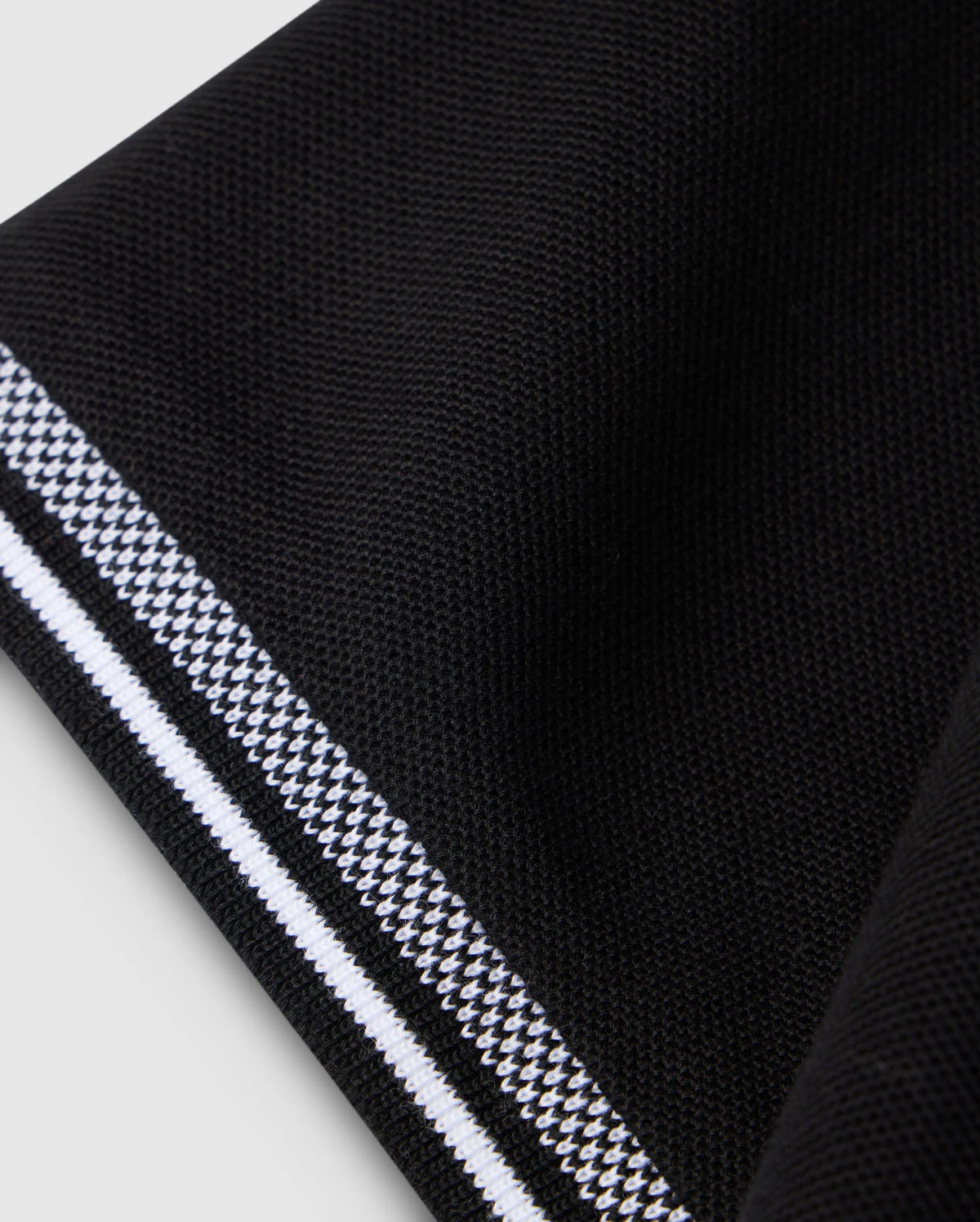 A close-up of folded black Pima cotton fabric with white and gray stripes along the edge resembles the textured surface of a Psycho Bunny Big and Tall Malton Pique Polo Shirt B9K950D200, highlighting its smooth folds and contrasting stripe.
