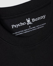 Close-up of the label on a black Psycho Bunny BIG AND TALL DUKE OVERSIZED TEE - B9U742D200, displaying the brand name with a rabbit skull logo. Made from heavyweight 100% Pima cotton and "Made in Peru," showcasing the quality of this relaxed-fit shirt.