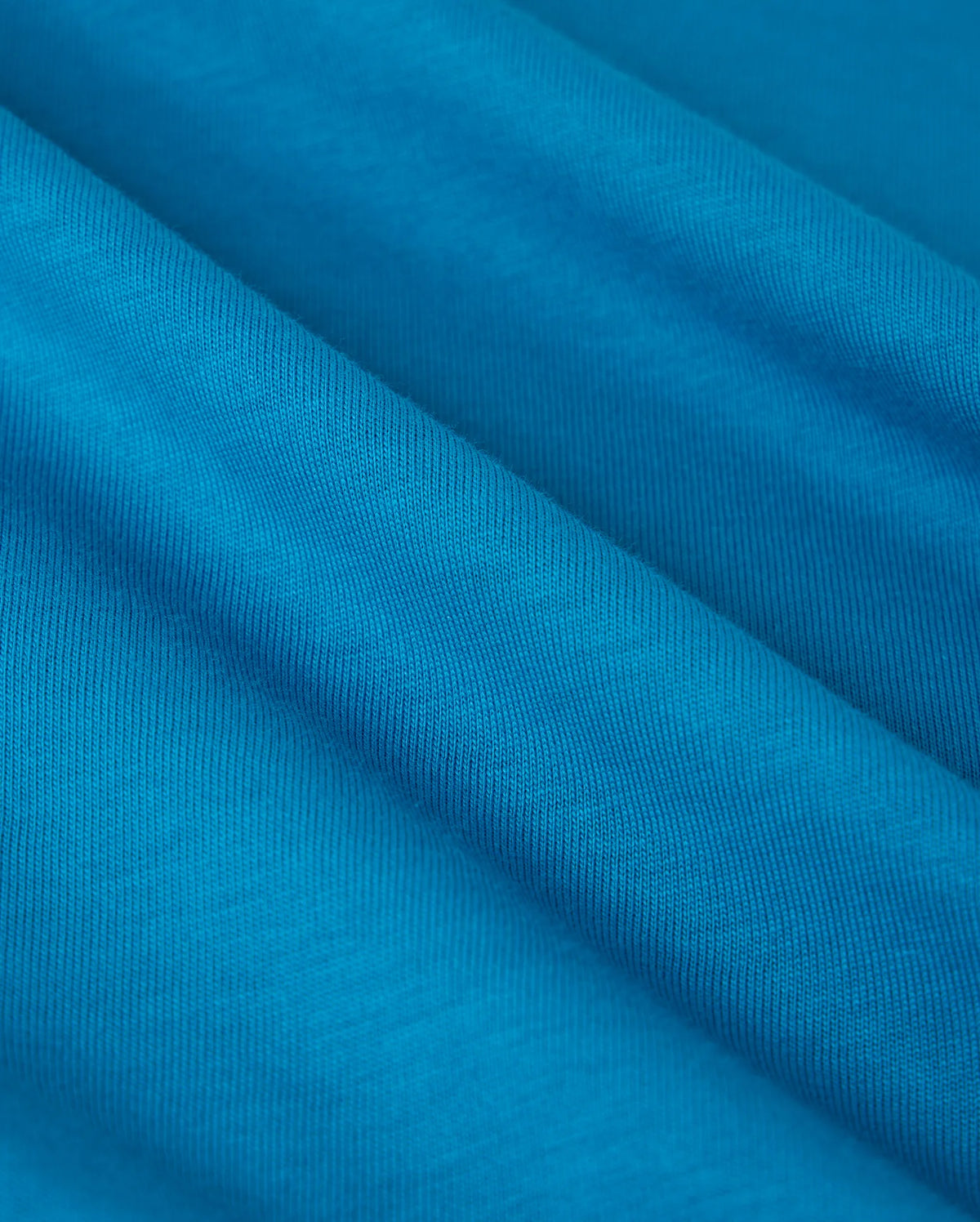 Close-up of the vibrant blue Pima cotton used in the Psycho Bunny BIG AND TALL MALTON GRAPHIC TEE - B9U795D200, featuring fine diagonal lines for a textured look. The soft fabric showcases Peruvian craftsmanship with gentle folds suggesting movement and fluidity.