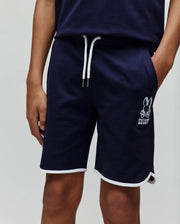 Kids Toby Short, navy French terry shorts with a relaxed fit, featuring white drawstrings, a large embroidered Psycho Bunny skull logo on the left leg, and white piping on the curved hem.