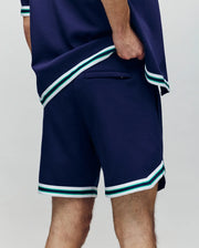 A person wearing Psycho Bunny MENS BASIL TAPED SHORT - MB0900005, featuring an elastic waistband and white and green striped trim, shown from the waist down and viewed from the side and back.